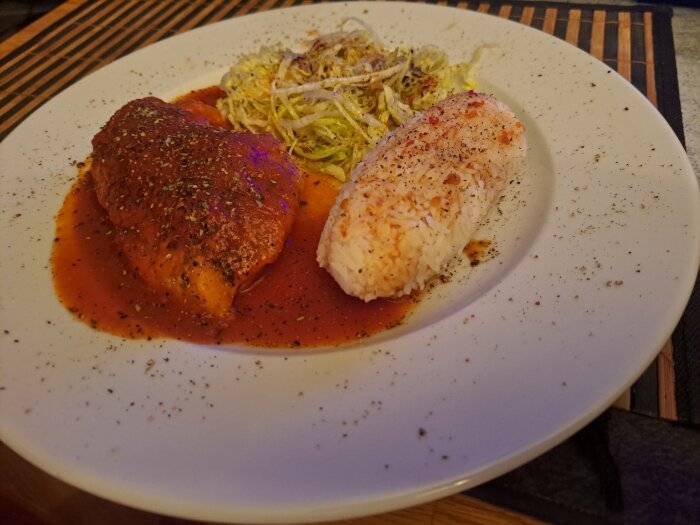Kycklingfilé med röd sås, ris och sallad serverat på en tallrik, kryddat med örter och peppar.