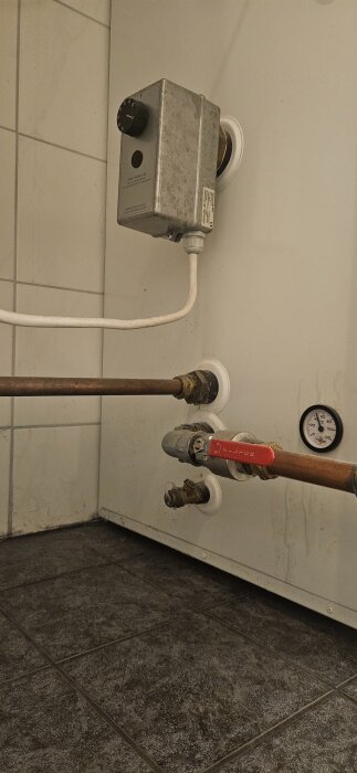 Ventil längst ner på panna, med röranslutningar och temperaturmätare, potentiellt för vatteninlopp.