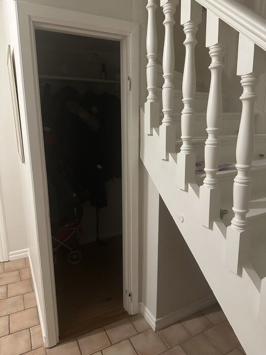 Dörr in till garderob bredvid en trappa med vita räcken; begränsat utrymme på grund av vägg och trappa.