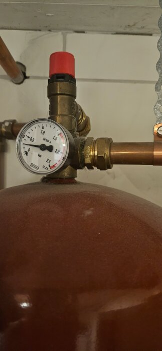 Manometer och ventil på ett rött expansionskärl med kopparrör i bakgrunden.
