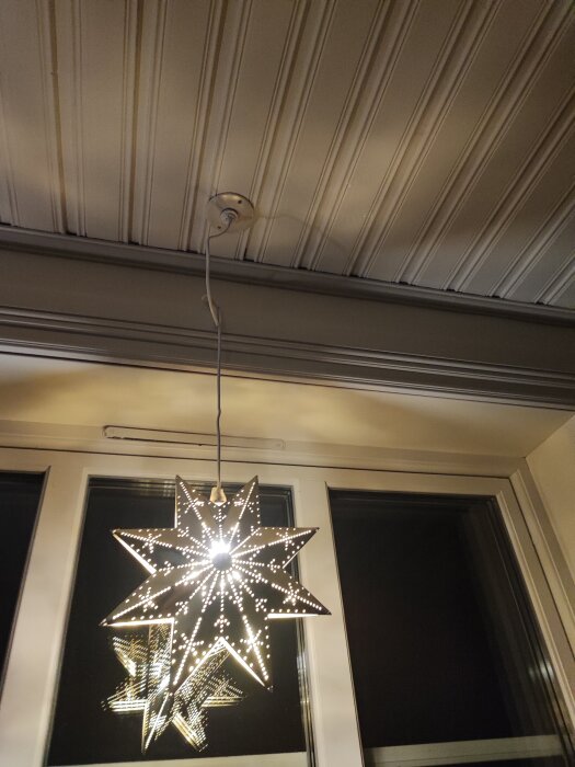 Lysande julstjärna i fönster, monterad i taket, avspeglar sig i glaset.