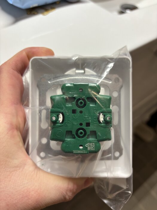 Vägguttag från Schneider Electric Exxact-serien, 2-vägs jordat med snabbanslutning, visas i en plastförpackning, hålls av en hand i ett badrum.