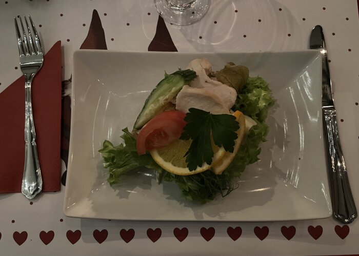 Smörgåstårta med kyckling, bacon, sallad och frukt garnerad med persilja på en vit rektangulär tallrik.