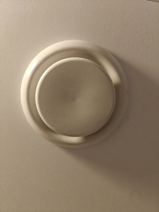 Rund ventilationsventil på en beige vägg.