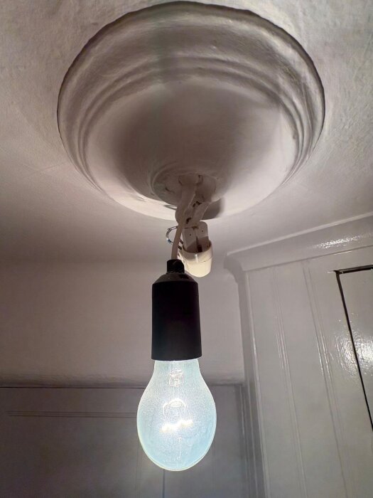 Takrosett med enkel hängande glödlampa och elkontakt mot vitmålat tak.