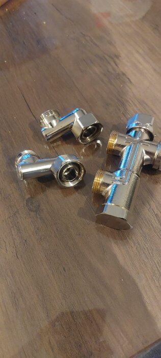 Tre metallkopplingar i mässing, liggande på ett trägolv. Fråga om tätning med lin eller gängtejp i forum för bygg och renovering.
