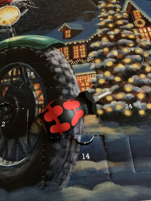 Skruvmejsel med röd och svart handtag ovanpå en adventskalender med julmotiv och siffror.