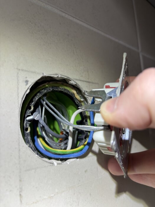 Elektrisk dosa med olika färgade kablar, inklusive svart, vit, blå, gul/grön och genomskinliga kablar, synliga på en vägginstallation.