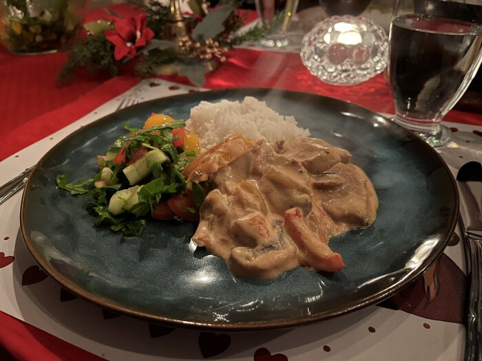 Krämig fläskfilégryta med champinjoner, lök, paprika och färskost serverad med ris och sallad, upplagd på en tallrik med juldukning.