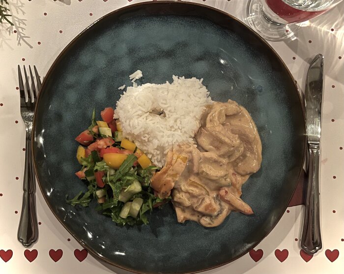 Krämig fläskfilégryta med ris och sallad på en tallrik, omgiven av bestick och duk i kärleksfullt tema.