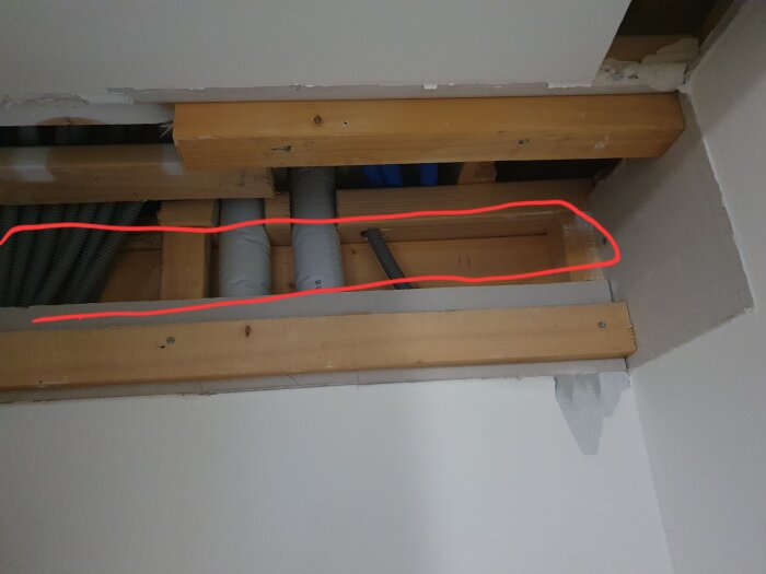 Öppning i en vägg visar träreglar och flera rör. Ett rött streck markerar en horisontell sektion med både el- och vattenledningar.