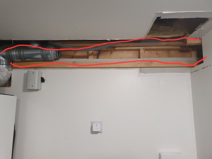 Öppen vägg med synlig träram och ventilationsrör, markerat med röd linje. Gipsplattor delvis borttagna för kanalinstallation.