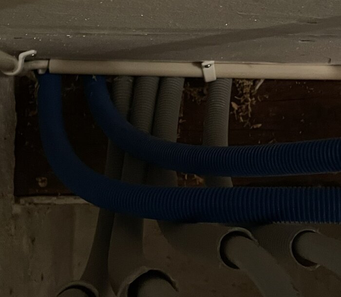 Blå och grå rör i en källare, sedda underifrån, delvis täckta av ett vitt plastlock.