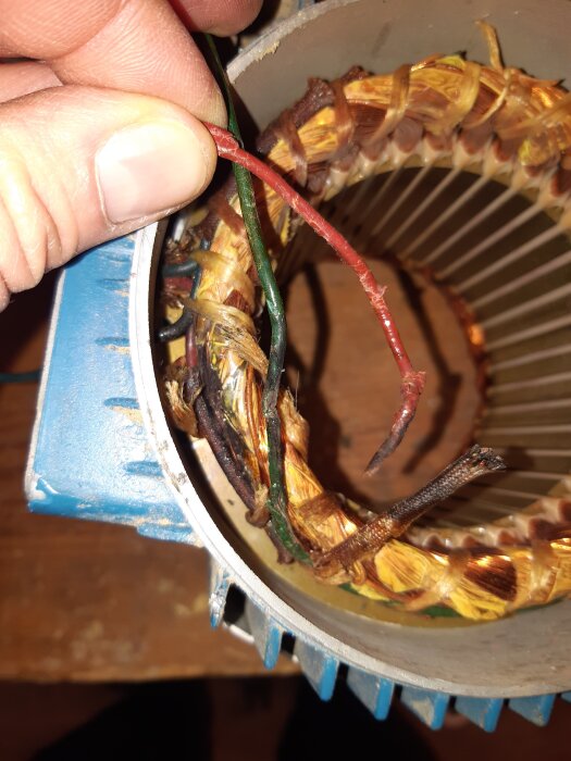 Närbild av en motorstator med synliga, delvis skadade ledare och lindningar, hållna av en hand.