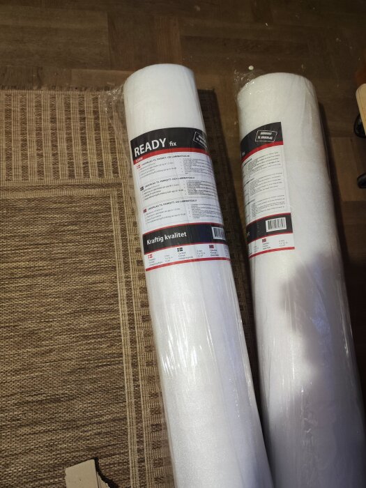 Rullar av underlagsmaterial "READY fix" för parkett och laminatgolv, märkta med "Kraftig kvalitet", utan aluminium på baksidan, ligger på ett golv.