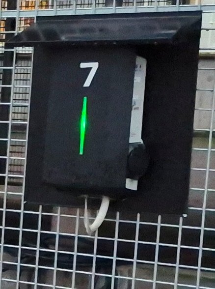 Laddbox fäst vid ett plank med metallgaller, märkt med siffran 7, har ett litet tak högst upp som väderskydd.