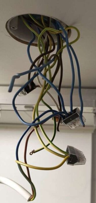 Exponerade elledningar hänger ner från ett takhål, med flera färger och anslutningskopplingar.