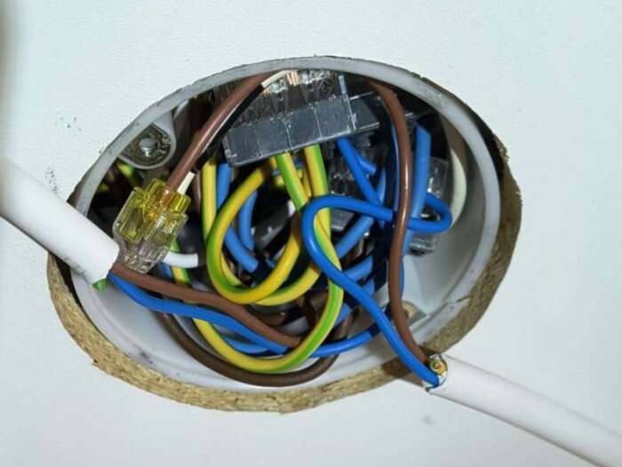 Elkopplingsdosa i tak med flera färgade ledare och kontaktklämmor, visar äldre installation som uppdaterats för mer utrymme och säkerhet.