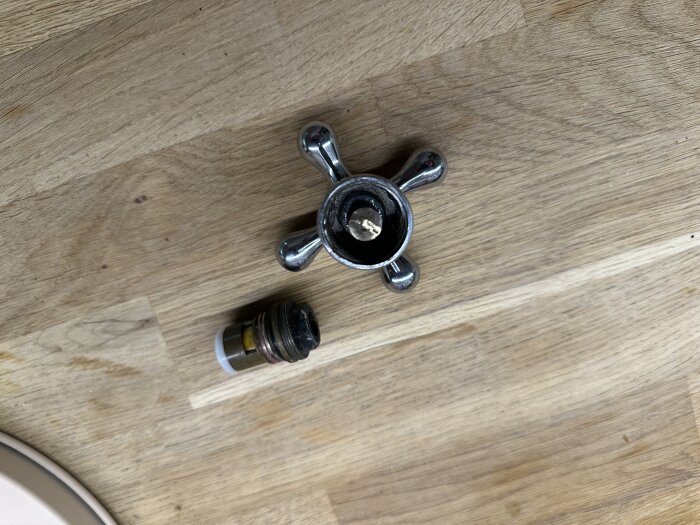 Ventiltopp och tillhörande del från en blandare ligger på ett träbord, utan synliga märkningar.