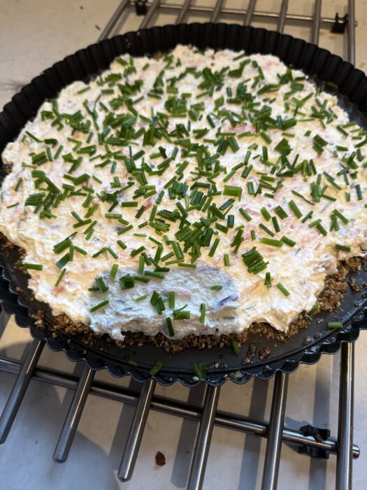 Cheesecake med räkor och rökt lax toppad med gräslök, serverad i en pajform med fröknäckebotten.