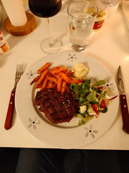 Grillad rostbiff med sötpotatispommes, sallad och sås på en tallrik, med ett glas rött vin bredvid.