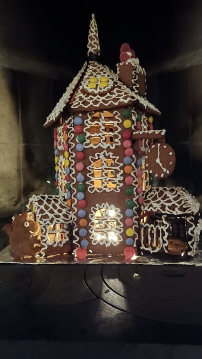 Dekorerat pepparkakshus med färgglada godisbitar och glasyrdetaljer, placerat på en mörk bakgrund.