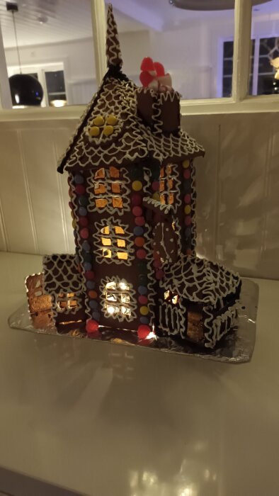 Pepparkakshus med dekorationer av glasyr och färgglada godisar, belysning från insidan.
