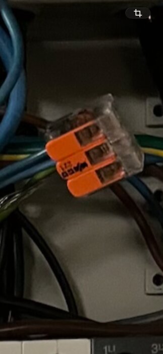 Orange kabelklämma ansluter flera elkablar i en elcentral, skyddsledare synlig.
