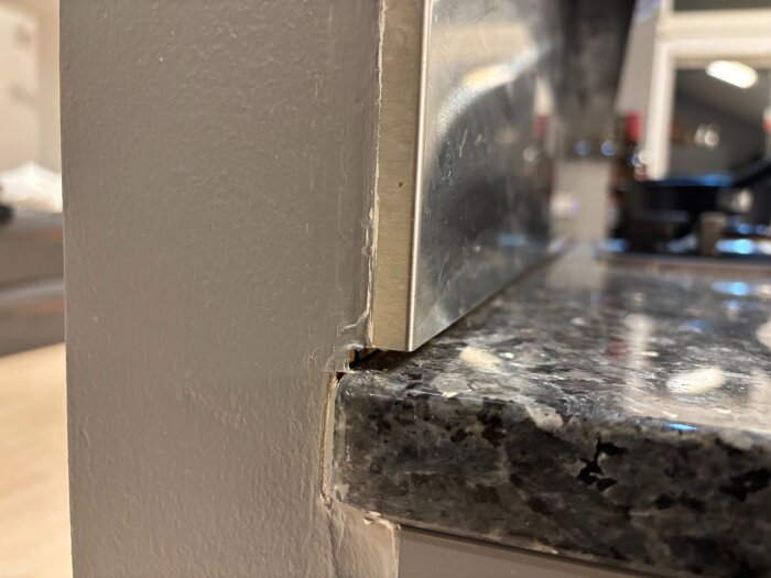 Glipa mellan köksbänkskiva i sten och rostfritt stänkskydd, vilket är en risk för att vätska kan rinna ner i väggen bakom.