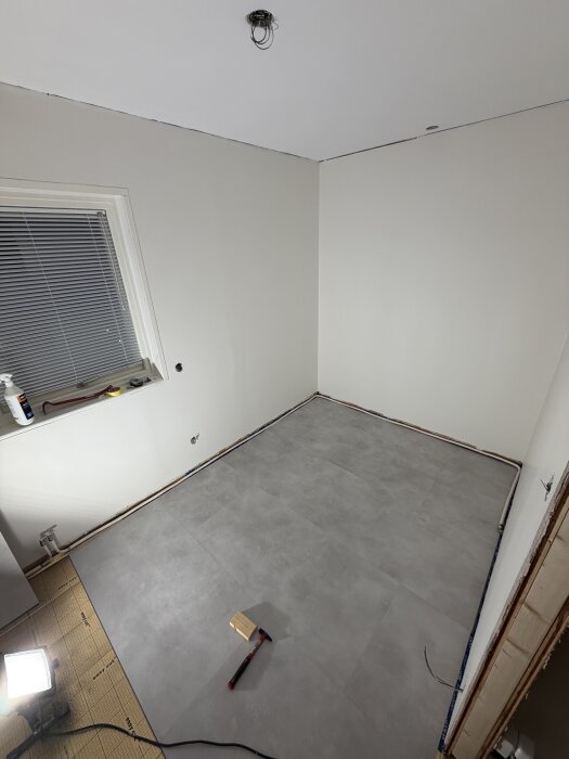 Blågrått vinylgolv i barnrum, delvis installerat, med bygglampa och verktyg i närheten. Väggar i äggskalsfärg.