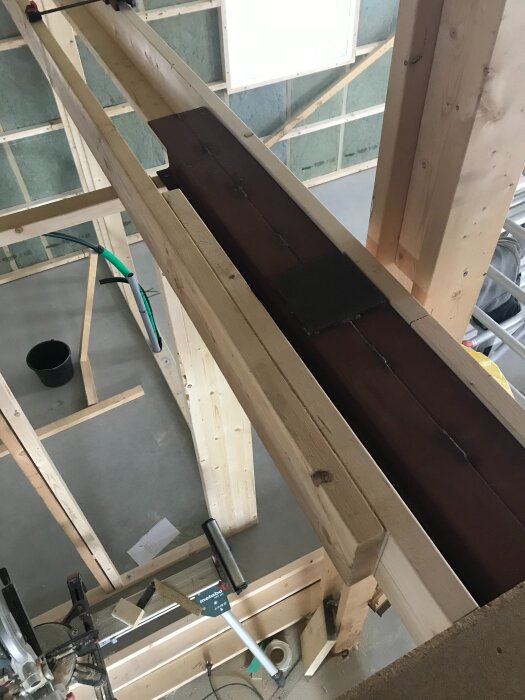 Träkonstruktion med en IPE160 stålbalk installerad som stöd för en nockbalk i ett fritidshus. Verktyg och material syns i bakgrunden.