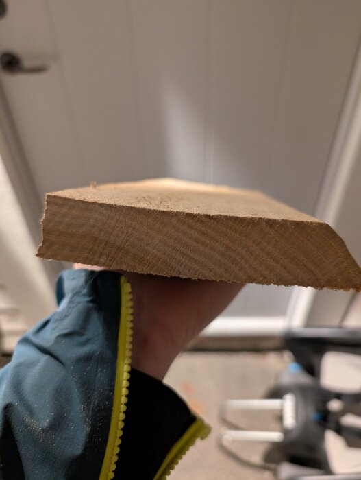 En person håller en träbit, möjligtvis bok, hittad i ett förråd. Träets yta är jämn och snittytan visas tydligt.