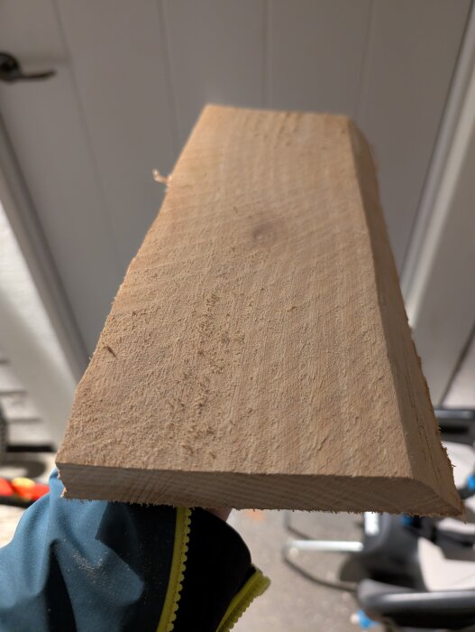 Träbit från farfars förråd, kanske bok, utan nämnvärd doft vid sågning, hålls i handen med grått och gult klädesplagg.