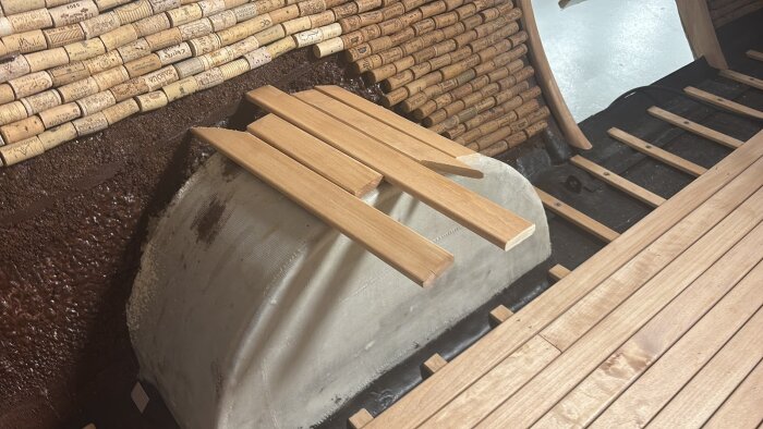 Träbitar placerade över ett hjulhus i ett renoveringsprojekt, omgivna av vinkorkar på väggen i bakgrunden.
