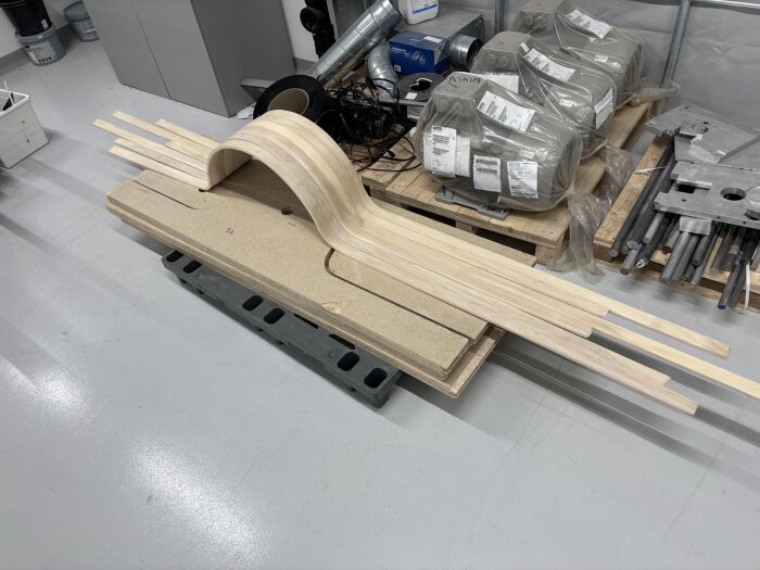 Formad träbit för hjulhus på arbetsbord i verkstad, omgiven av material och utrustning. Biten är böjd och tillverkad genom basning.