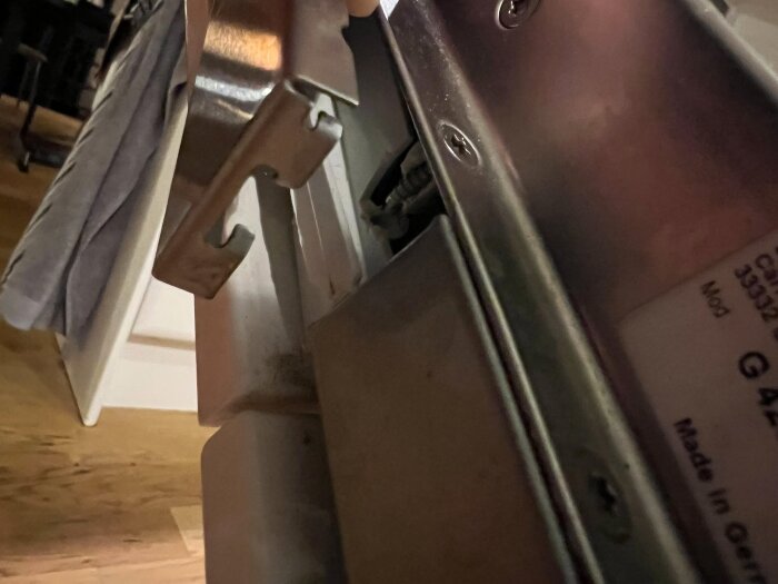 Närbild av en delvis öppen diskmaskin med fokus på en metallskena och ett skadat fäste på styrenhetens kåpa.