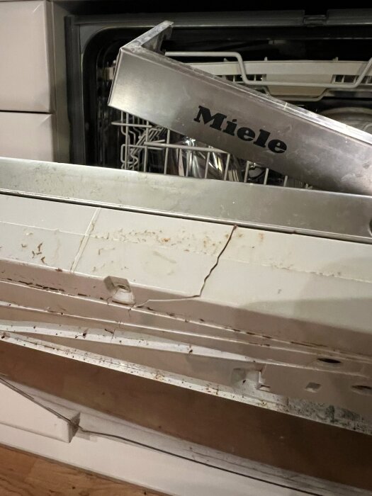 Sprucken kåpa på Miele diskmaskin från 2014, med vertikal spricka och rost på korgar synliga. Kåpan dras ut vid öppning.