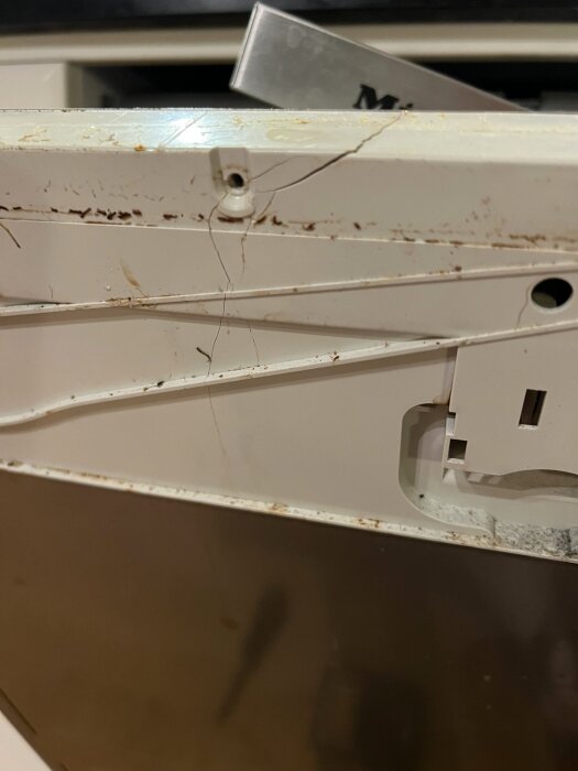 Spricka i styrenhetens kåpa på en integrerad Miele-diskmaskin. Kåpan visar skador runt infästningar och rostiga delar.
