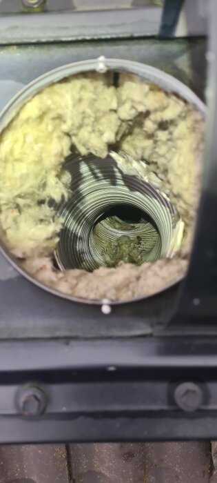 Insidan av ett metallrör med isolering, delvis tilltäppt vid skarven, nära taket. Rör skadat, orsakar problem med köksfläktens luftflöde.