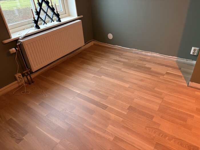 Hörn av rum med parkettgolv, eluttag och radiator under fönster. Blottad golvlist för eventuell kabeldragning diskuterad i forumtråd.