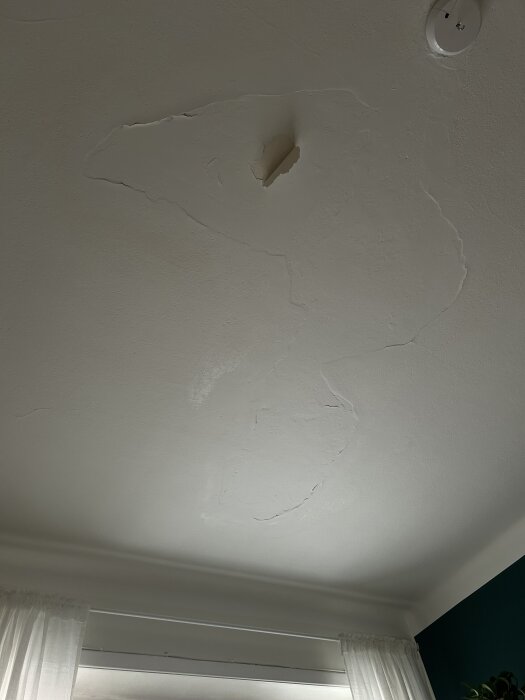 Spricka i taket ovanför fönstret med synliga skador och en rökdetektor monterad nära, del av ett renoveringsprojekt.