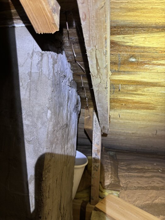 Vattenläcka i ett hus, synligt vid takbjälkar och vägg, med en hink placerad under för att samla droppande vatten.