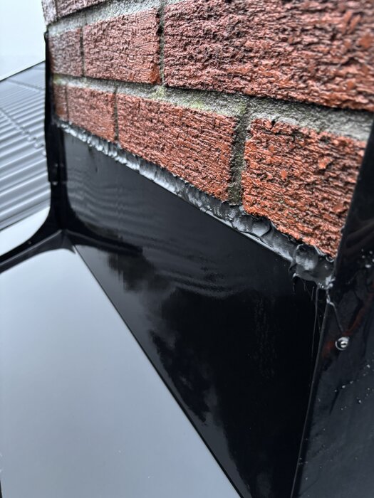 Röd tegelvägg med svart tätning där vatten kan tränga in vid takanslutning.