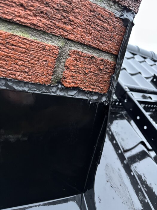 Röd tegelvägg möter svart takplåt med tätning. Möjligtvis läckagepunkt upptäckt vid regn i nytt hus.