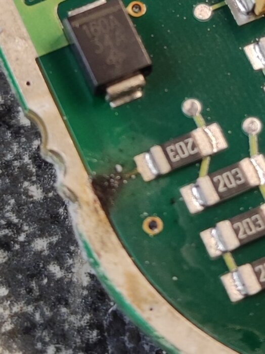 Elektronisk krets med motstånd och en IC-komponent på ett grönt kretskort, visar brännmärken och skador nära kanten.