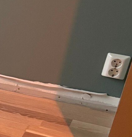 Vägg med dubbelströmuttag och synlig kabel vid golvlister.