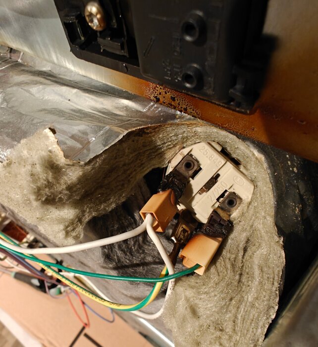 Bränd inre komponent av en elektrisk apparat, med synliga kablar och smält kontakter, troligen relaterad till en ugn eller fläktmotor.