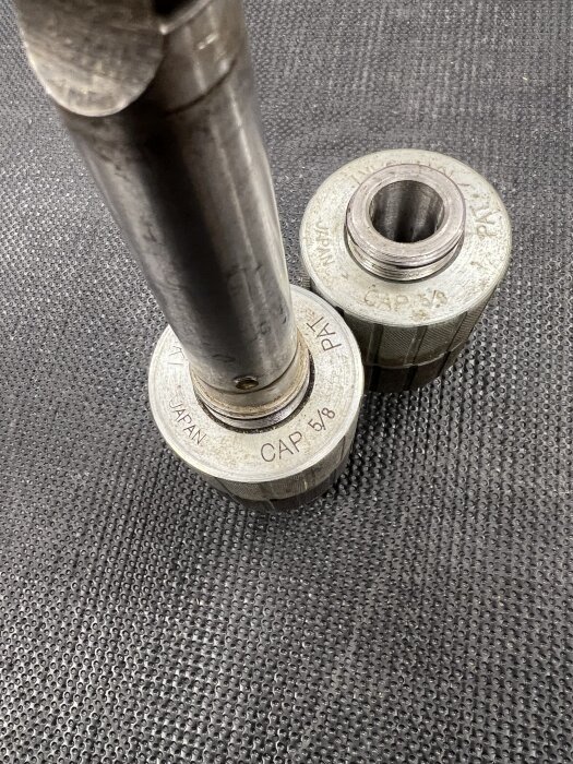 Två borrchuckar märkta "Kawasaki CAP 5/8", en med axel och en lös, på en mönstrad yta.