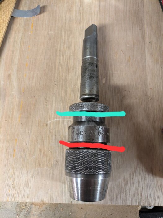 Borra chuck med röd och grön linje markerad för demontering och åtdragning, ligger på ett träbord.