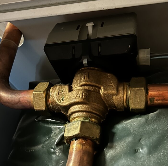 Bilden visar en kopparrörsanslutning till en fördelningsventil i brons för VVS-installation, som är monterad i ett trångt utrymme.